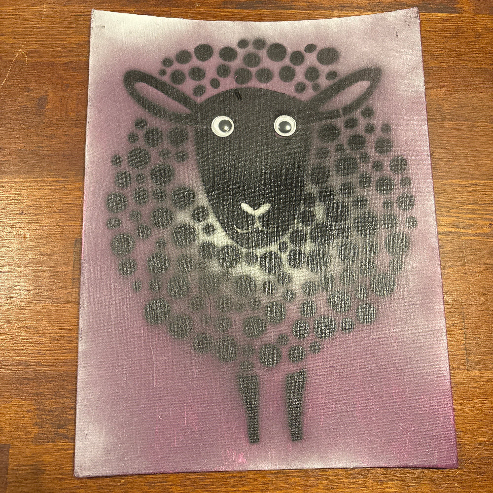 A square art print or card featuring a stylized black sheep face and body made of dots on a dusty purple background, photographed on a brown wooden surface.
